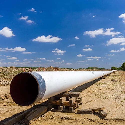 A large white pipeline elevated above freshly excavated dirt in an open field. The pipe runs at least 200 yards into the distance.