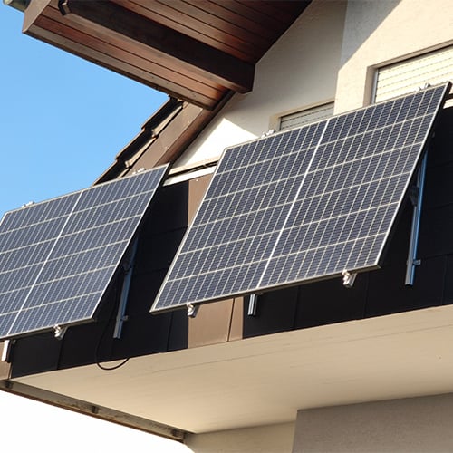 Two solar panels mounted to a balcony on a modern single-family home.