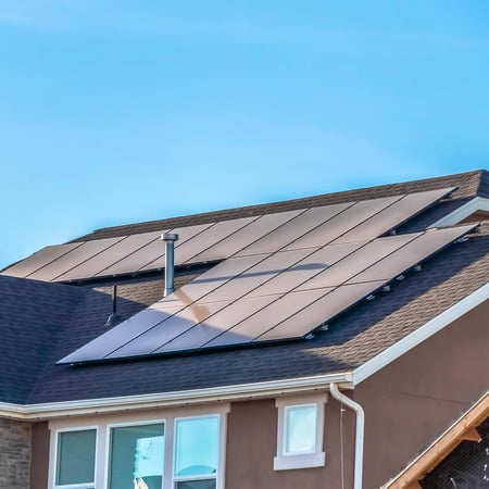 A collection of solar panels on the rooftop of a single family home on a sunny day.