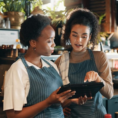 Two staff members gather around a tablet and stand behind a bar in an upscale restaurant.