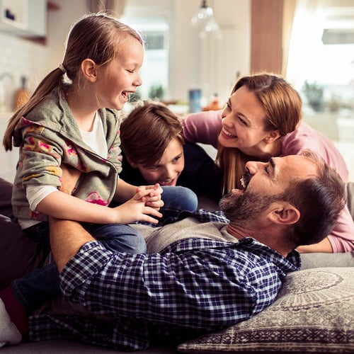 Four members of a family embrace and smile together on a couch.