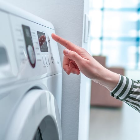 A hand pressing a button on a clothes dryer.