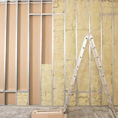 A ladder in front of a wall under construction, which has half of the installation installed.
