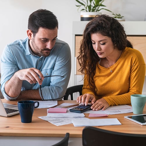Una pareja se sienta a la mesa de la cocina con una calculadora y un ordenador portátil para pagar una factura.