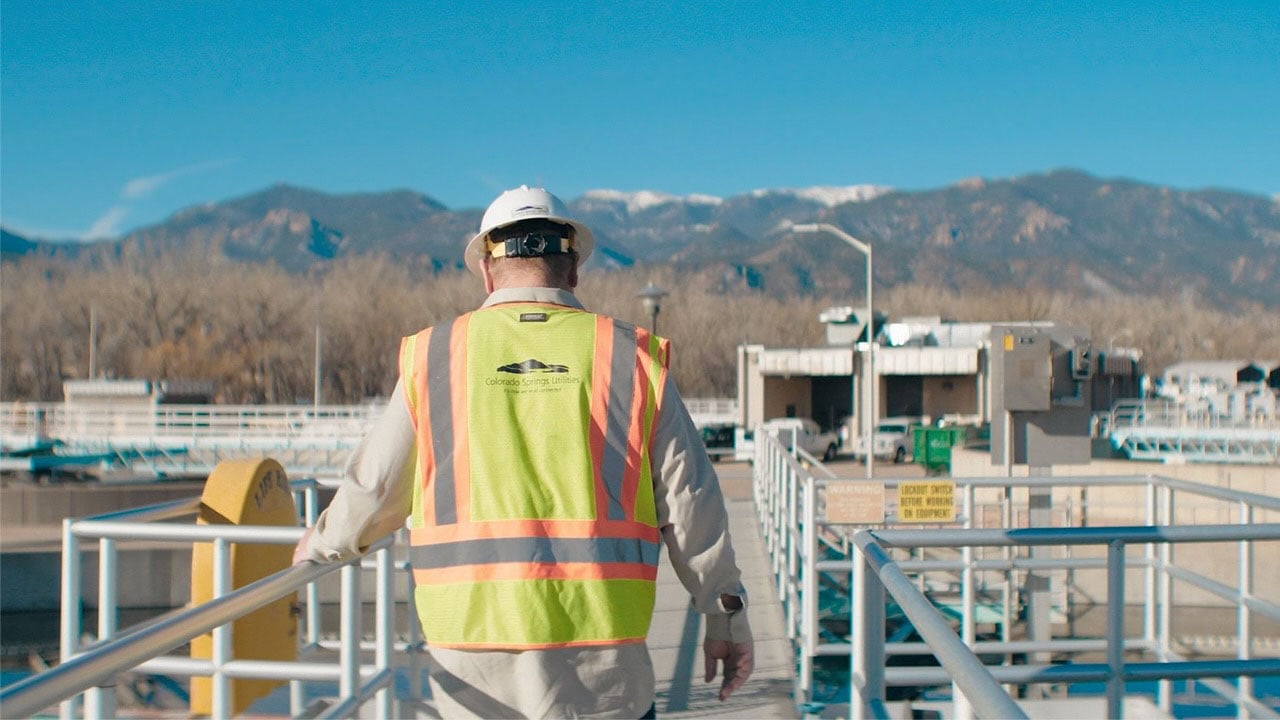 A utilities employee standing in an industrial site with mountains in the background.