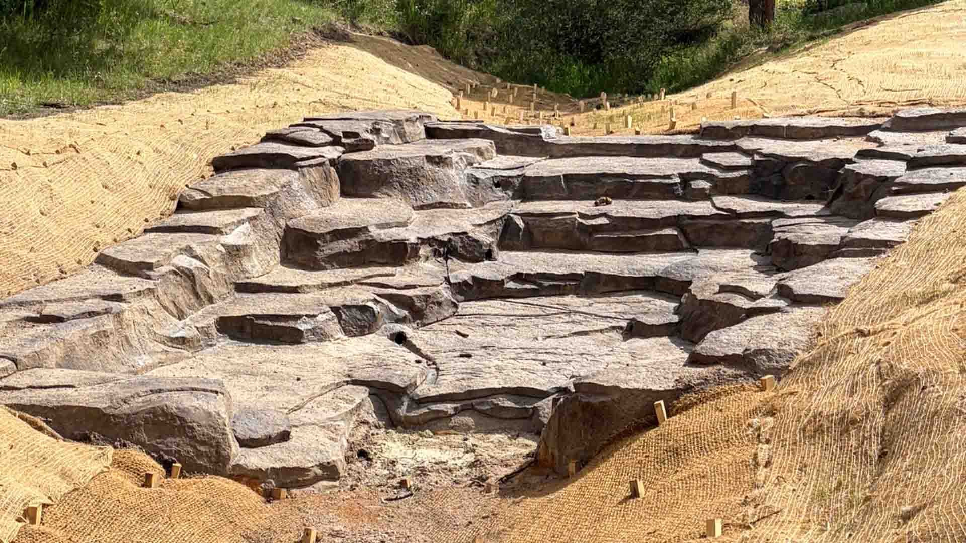 A completed concrete drop structure in a creek bed. Yellow straw matting is visible around the area