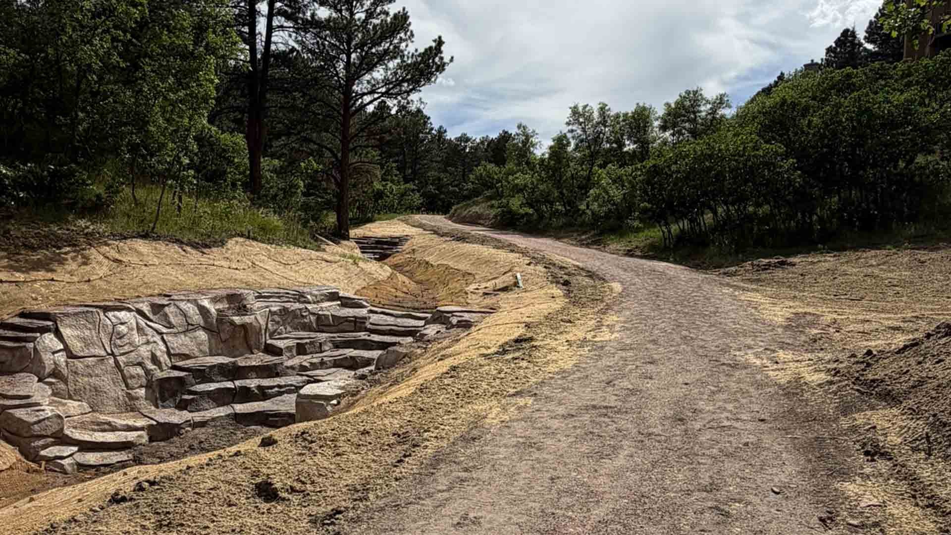 Trail next to  a reconstructed drainage channel lined with large stone features and straw mats.