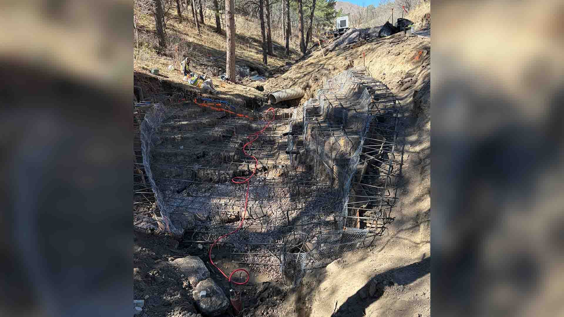 A large rebar frame is built in a dry stream bed in a wooded area ahead of concrete installation.