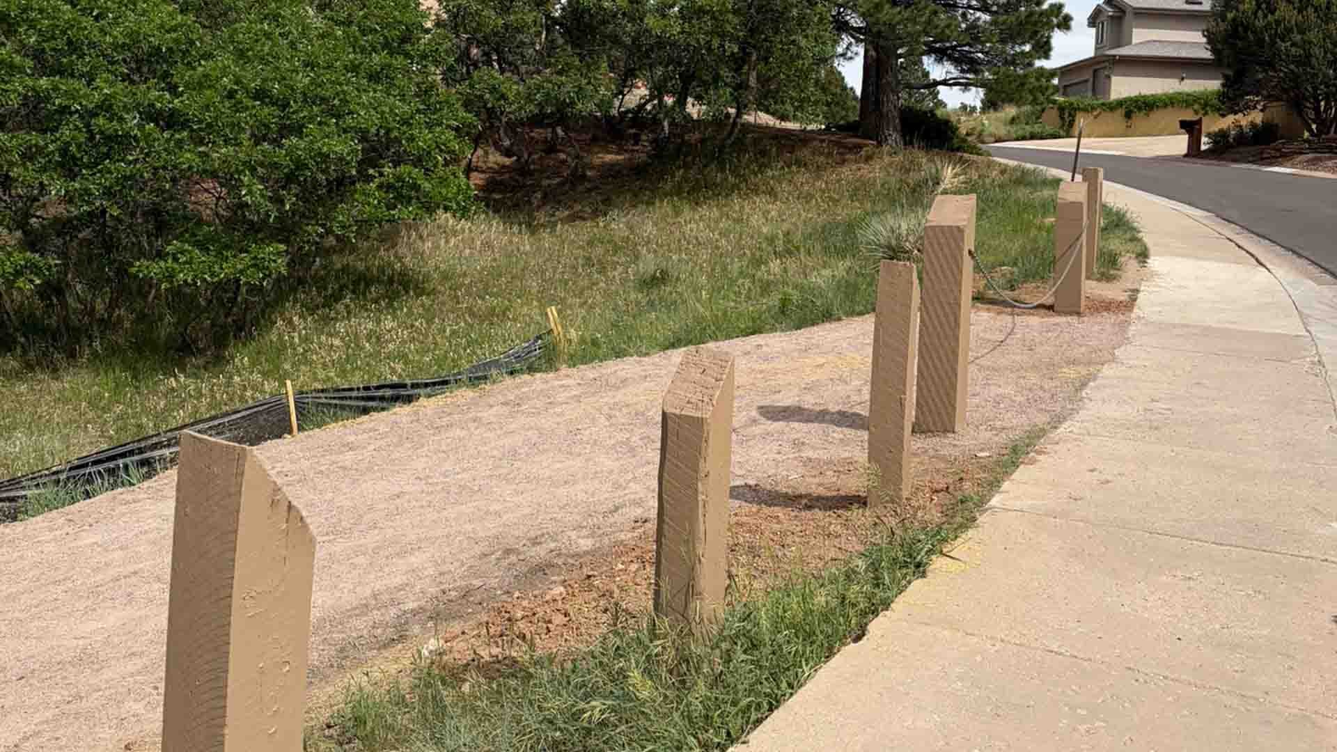 A gravel trail sits next to a residential street and sidewalk. There are wooden bollards and a cable barrier installed for safety.