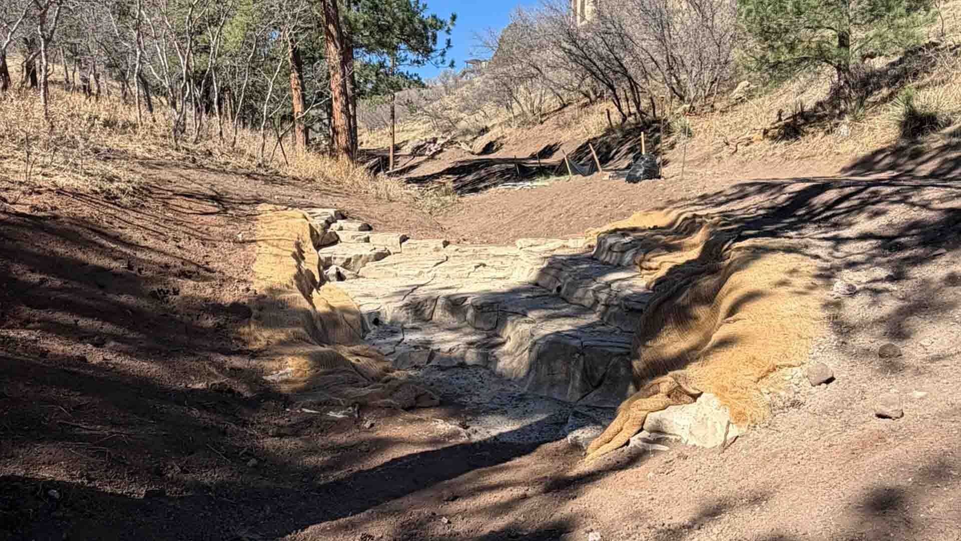 Stepped rock stabilization structure in a drainage channel within a wooded area, designed to manage stormwater flow and reduce erosion.