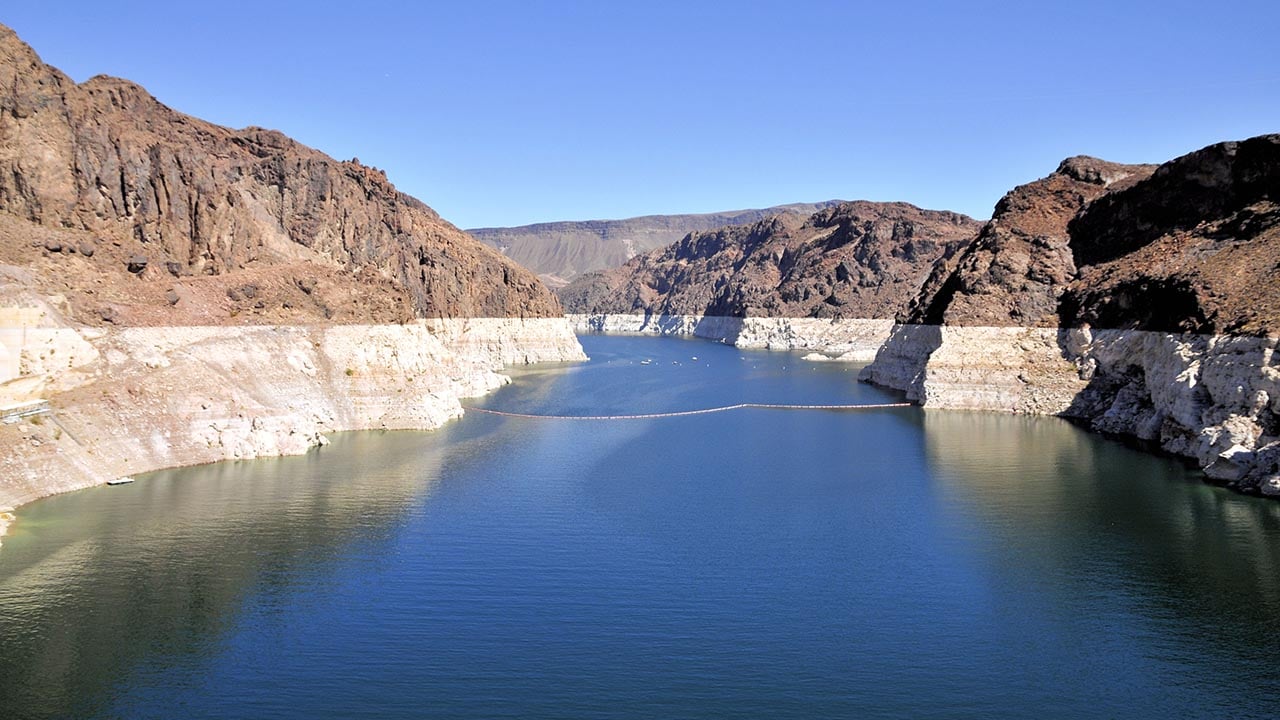 Lake Mead with a low water level. There is a clear "bathtub" ring illustrated by rock that is white compared to brown rocks above the old water level. It's a dramatic illustration of how much water has been lost from the reservoir.