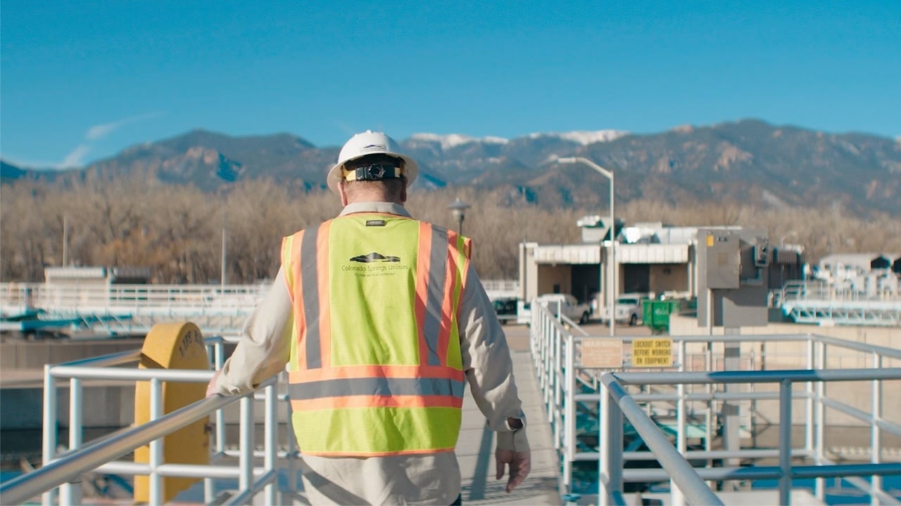 A utilities employee standing in an industrial site with mountains in the background.