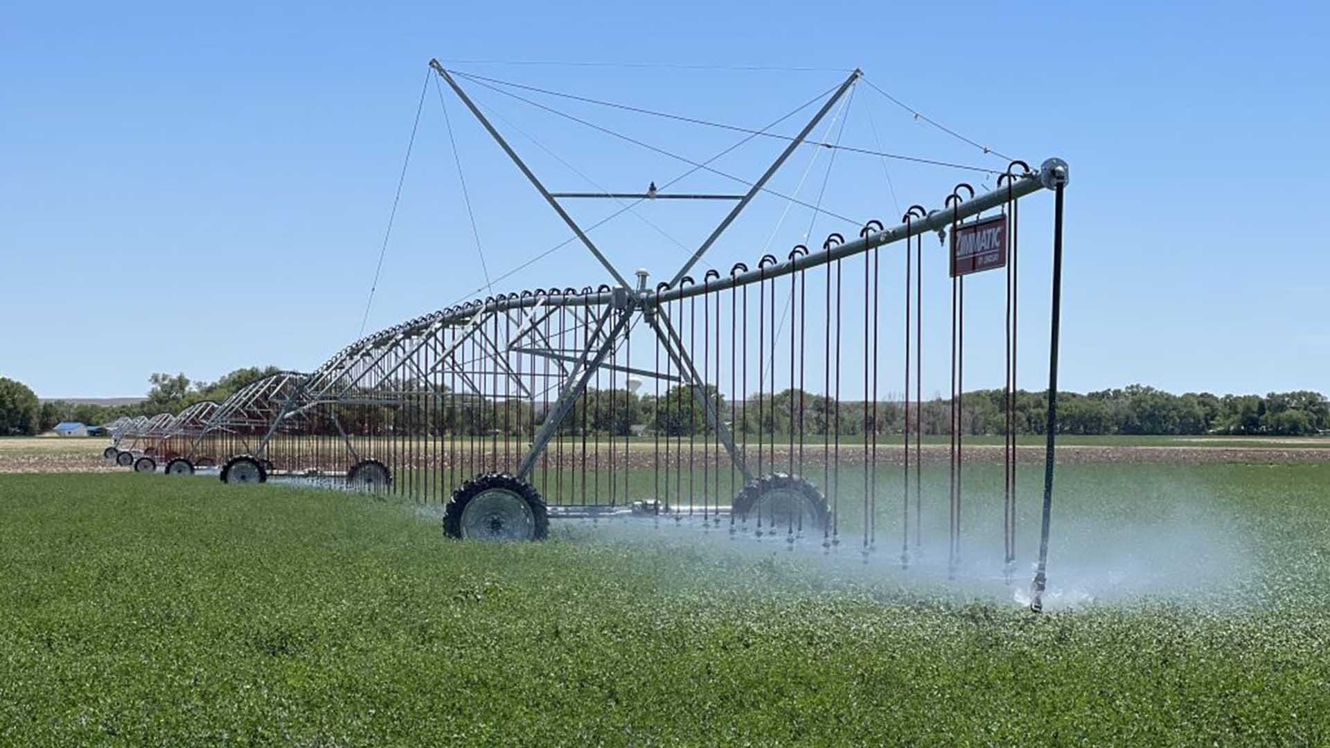 A large agricultural irrigation system watering a green field under a clear blue sky.