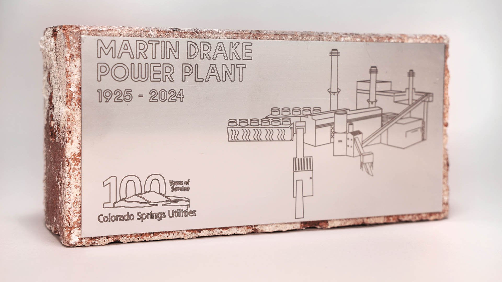 A brick with a plaque attached to the front. The plaque reads "Martin Drake Power Plant 1925-2024" and includes an outline of the old structure.