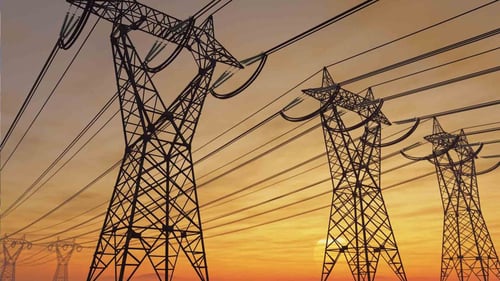 Photo of 3 high-voltage transmission towers with power lines stretching across the sky during sunset.