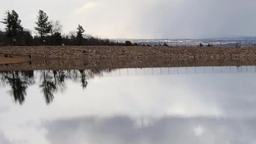 Photo of a small pond on a cloudy day. A sign that reads "no fishing, no human swimming" is placed in the foreground on a sandy beach.
