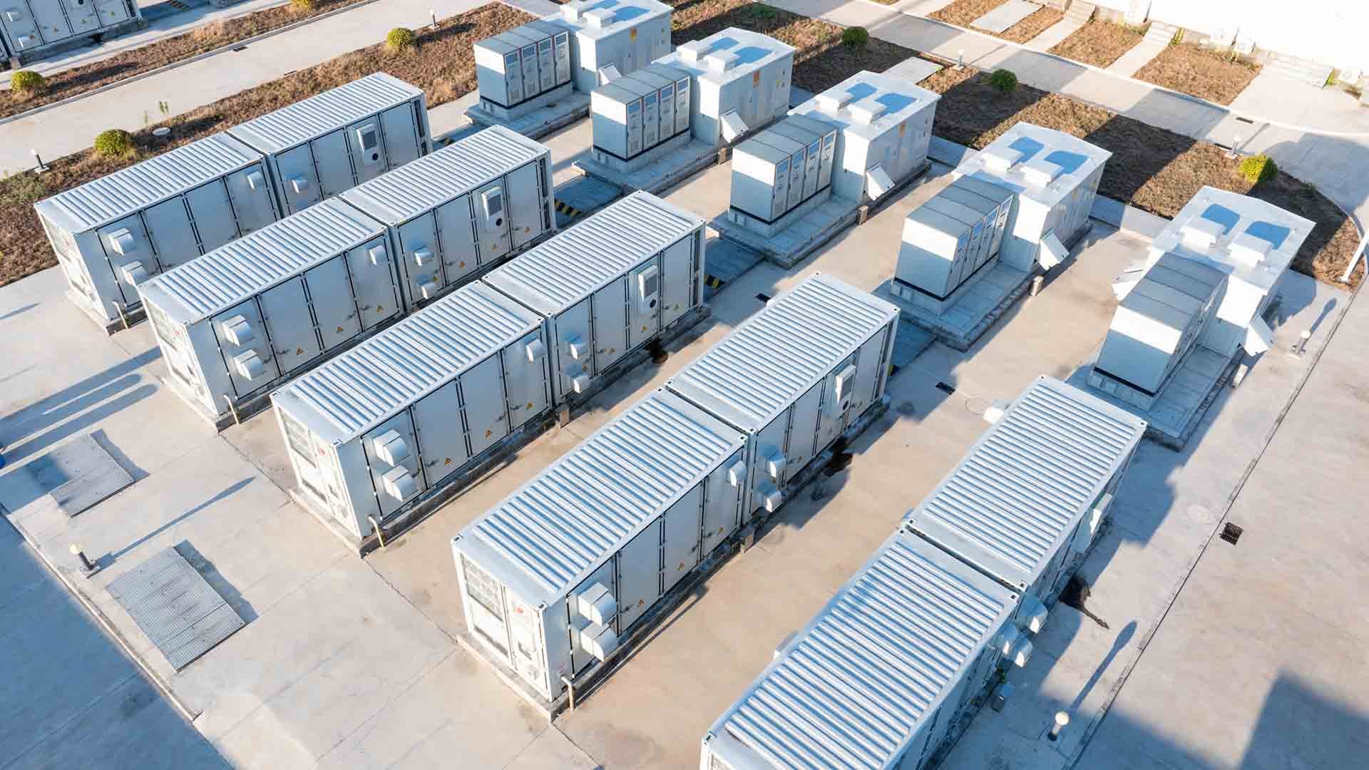 A representation of five battery electric storage units photographed from an aerial angle. They are light grey and look similar to shipping containers.