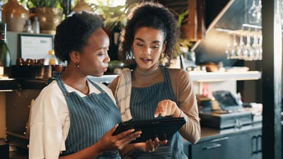 Two staff members gather around a tablet and stand behind a bar in an upscale restaurant.