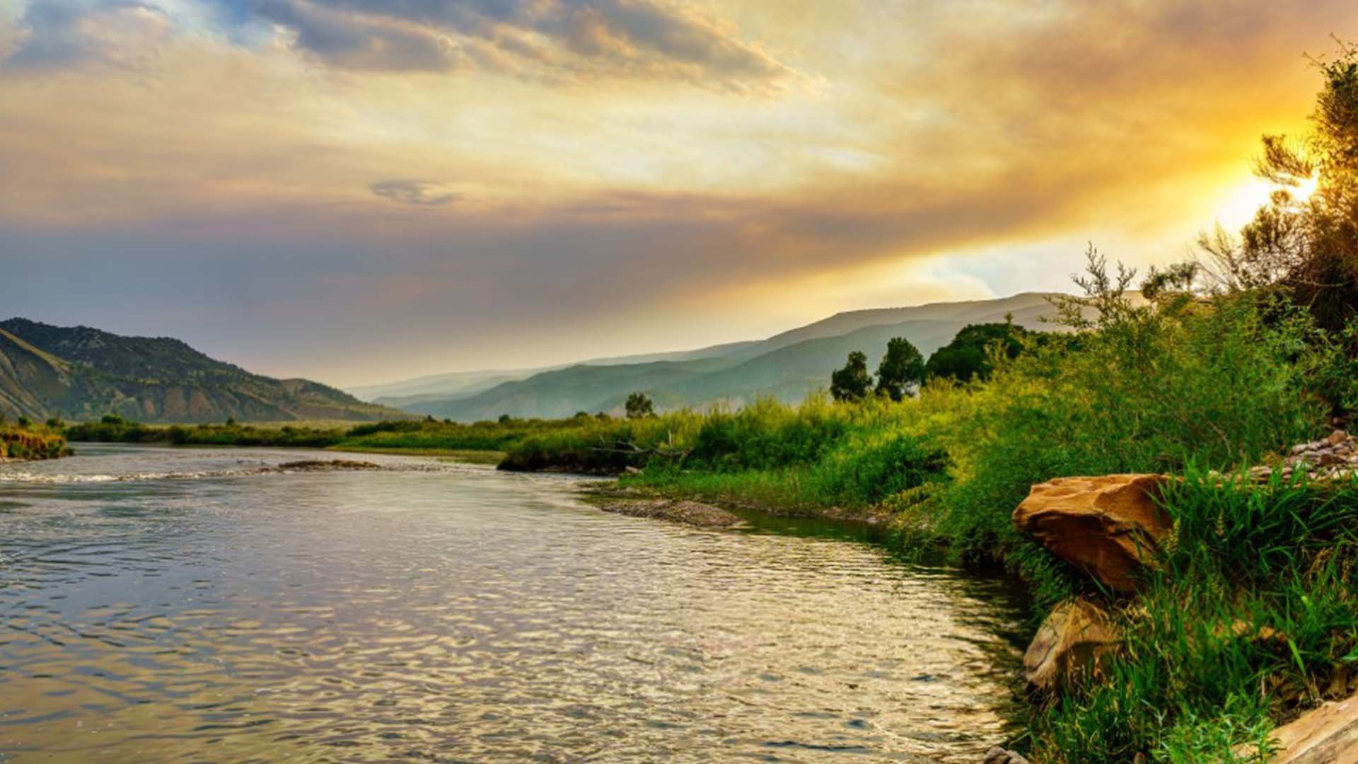 The Colorado River flowing through a mountainous landscape under an orange sunset.