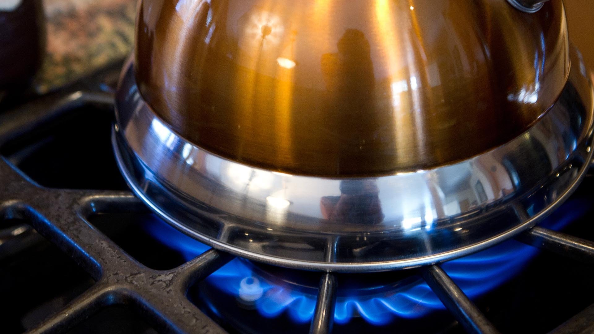A teapot sits on a burner with blue flames fueled by natural gas beneath it on a stovetop.