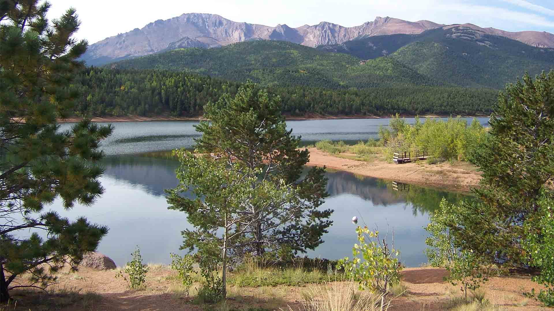 Shores of North Catamount Reservoir, a serene lake with calm blue waters and Pikes Peak towering over it in the background.