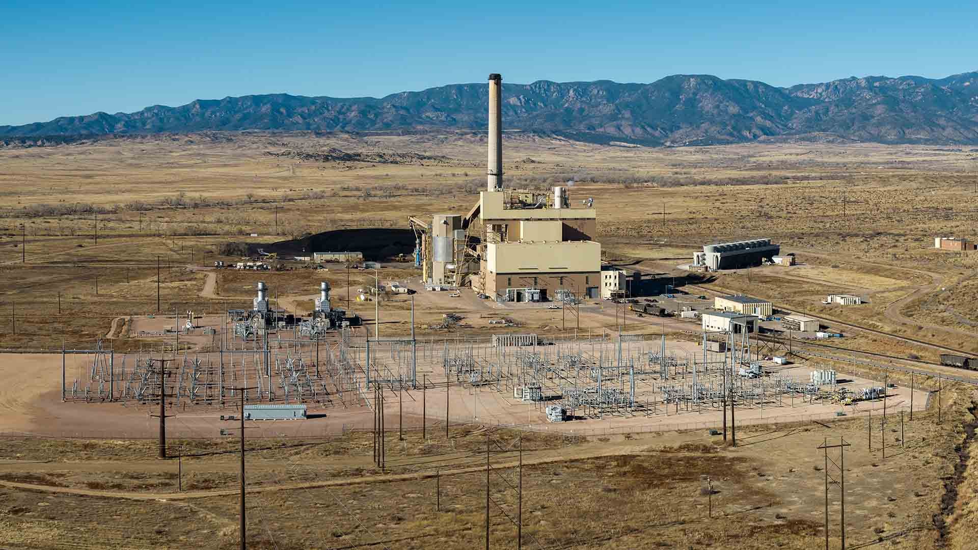 Aerial photo of a coal power plant with a tall stack and large tan building surrounded by power lines and infrastructure surrounding the structure.