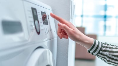 A hand pressing a button on a clothes dryer.