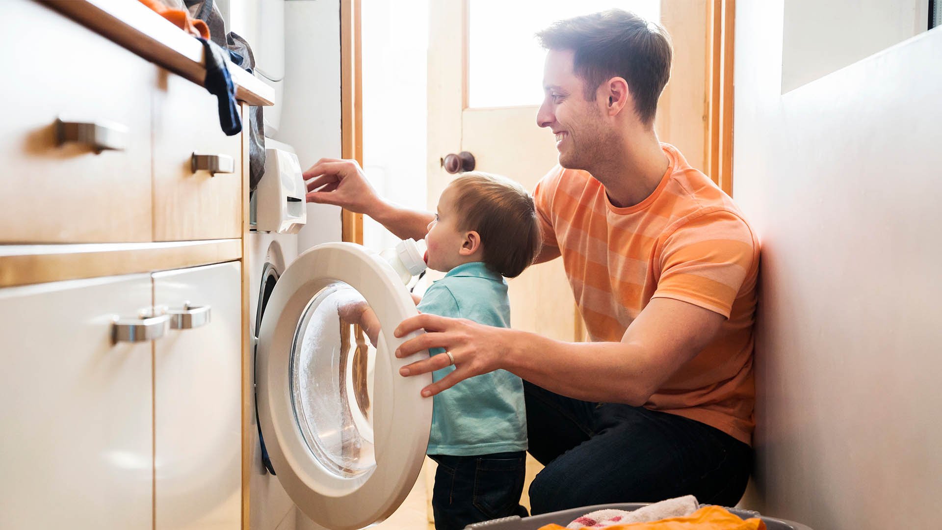 A father and toddler son unloading laundry from a clothes dryer together.