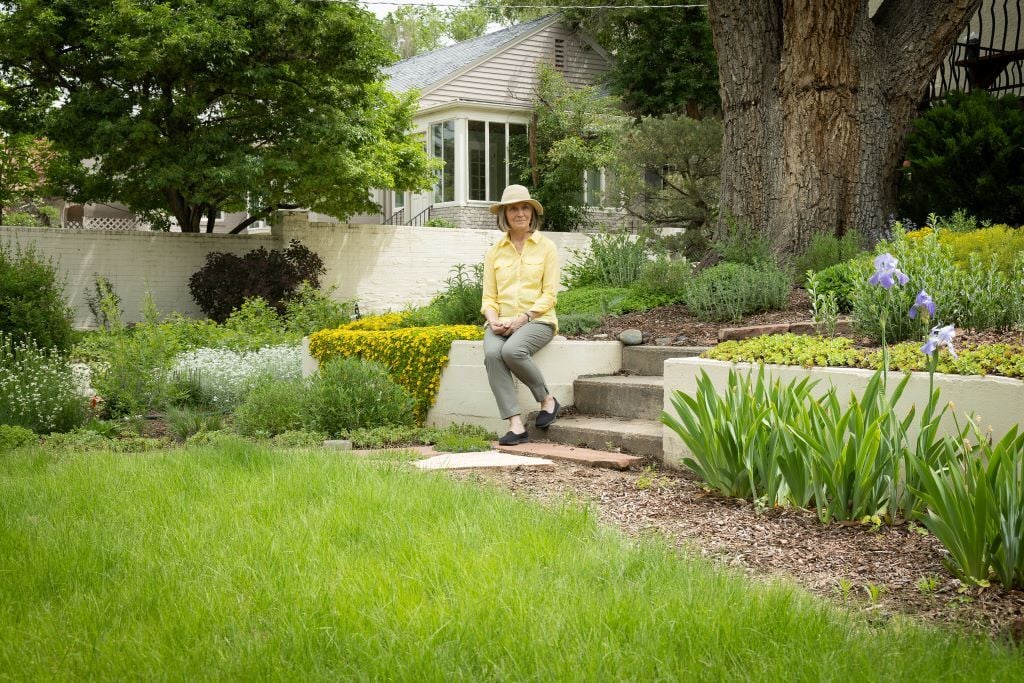 A woman sitting on a retaining wall, with a green lawn in front of her.