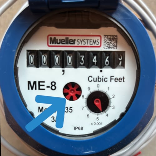 Water meter with an arrow pointing to a small red cog in the center of the meter.