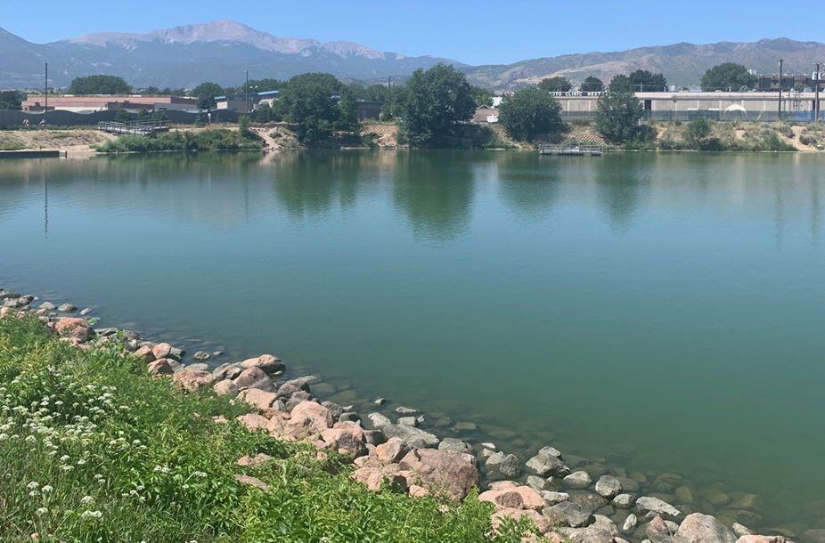 Green colored water inside a small lake with Pikes Peak in the background.