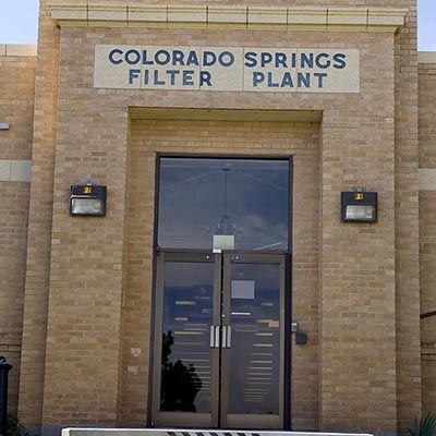 The entrance to a brick building with the words "COLORADO SPRINGS FILTER PLANT" above the glass doors.
