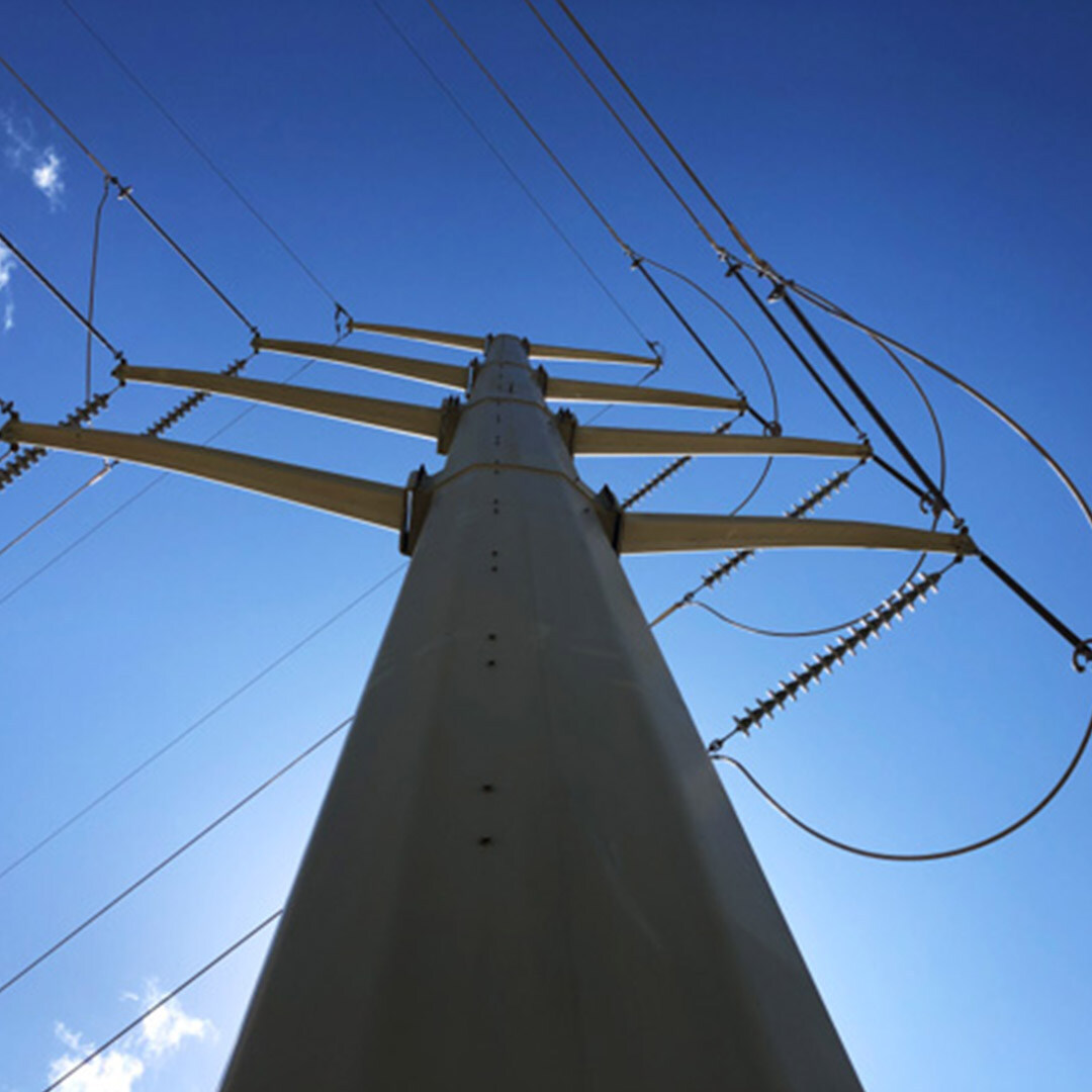 A large steel power pole photographed from the base of the structure looking up. Powerlines are strung from each arm of the structure.