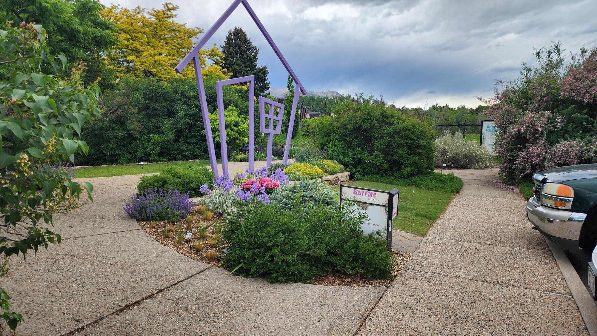 A natural plant landscape with a purple home shaped piece of art.