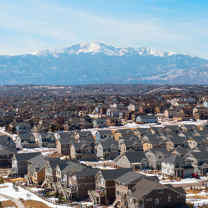 Suburban single-family homes stretch into the distance. Snow is visible on Pikes Peak and on yards in the background, indicating a cold day.