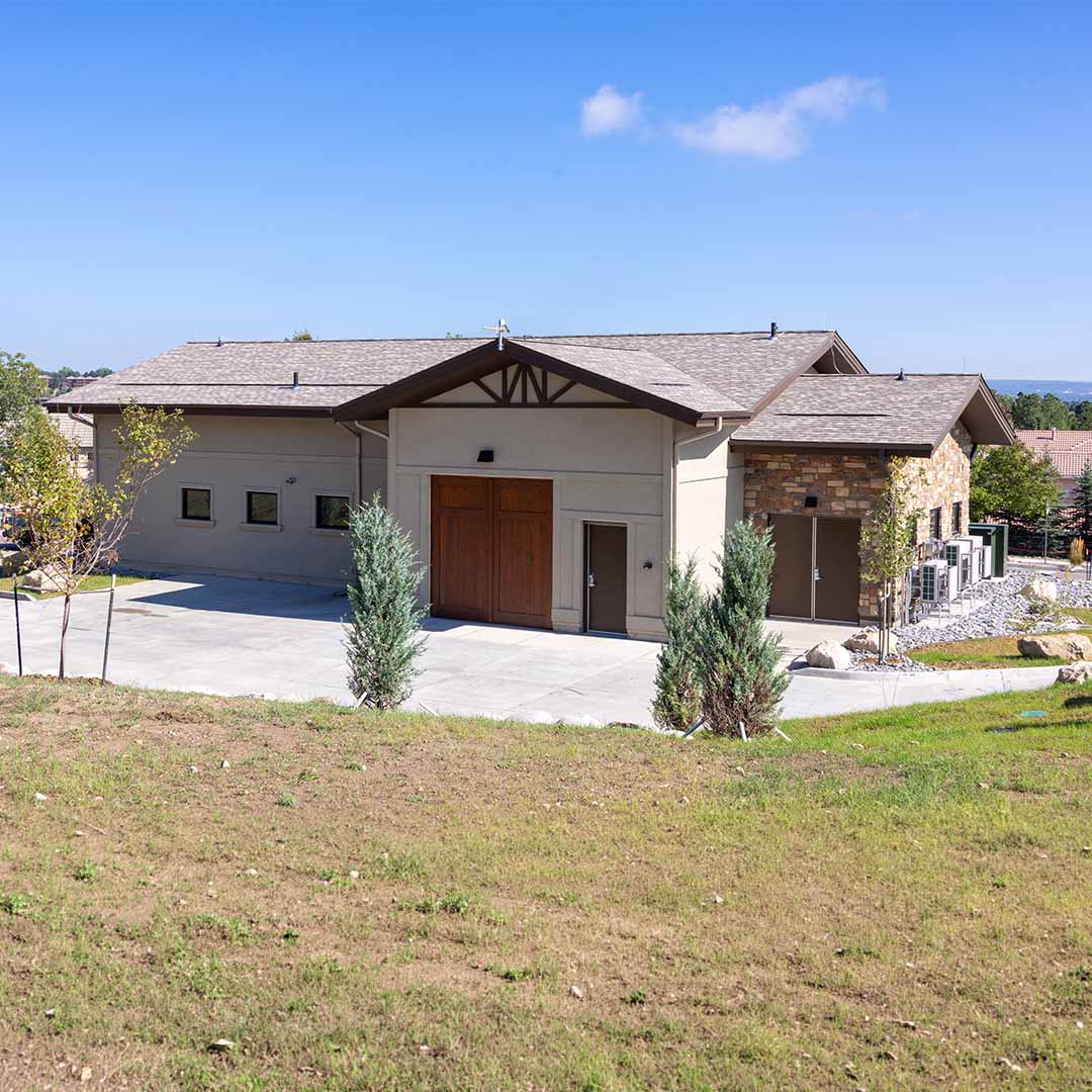 A stucco building resembling a suburban, single-family home with a driveway and landscaping surrounding it.