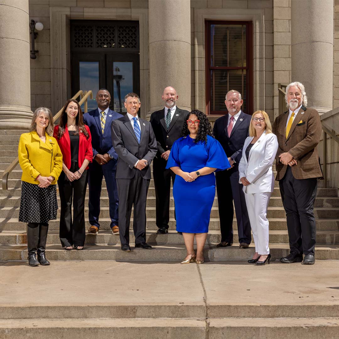 A group photograph of Colorado Springs Utilities Board members on the steps of city hall. Members pictured from left to right are Nancy Henjum, Brandy Williams, Roland Rainey, Brian Risley, Dave Donelson, Kimberly Gold, Tom Bailey, Lynette Crow-Iverson and David Leinweber.