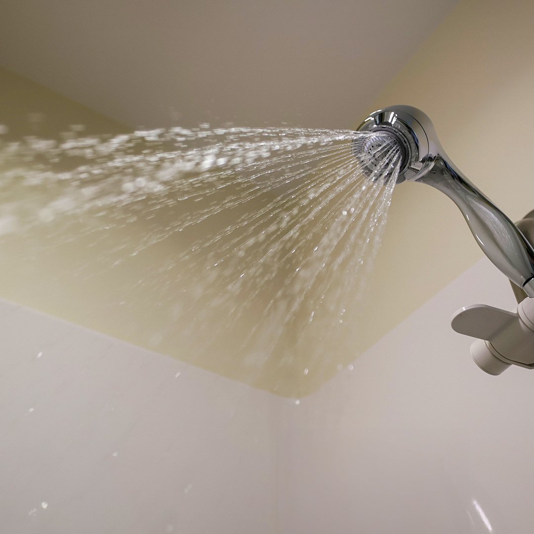 Cabezal de ducha plateado que rocía un amplio abanico de agua en una cabina de ducha.