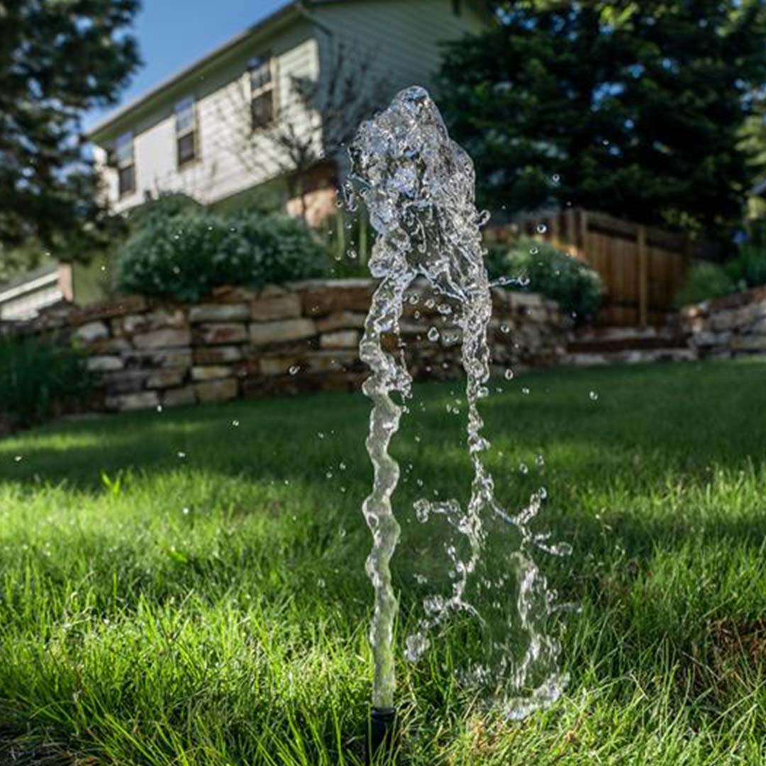 Un aspersor roto lanza agua al aire sobre un césped verde.