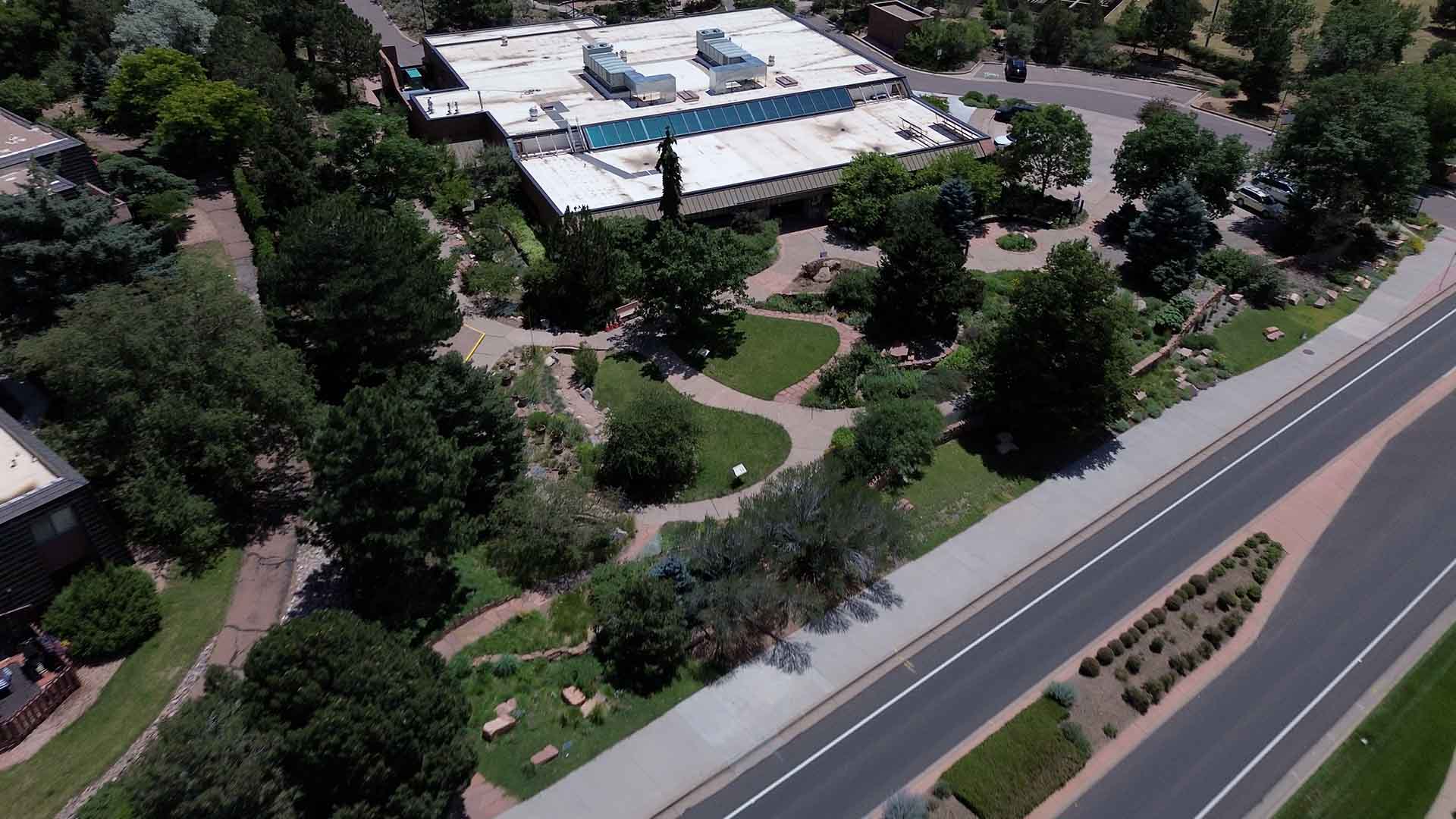 Aerial image of the Colorado Springs Utilities Conservation & Environmental Center. There is a large green garden with multiple pathways in front of a building with a flat white roof.