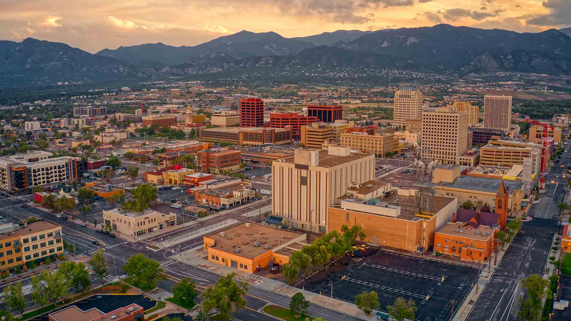 Aerial photo of downtown Colorado Springs at sunset. There is an orange glow in the sky, indicating high clouds or a recent rain.