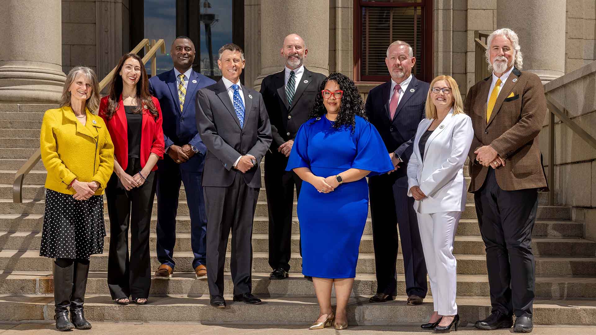 A group photograph of Colorado Springs Utilities Board members on the steps of city hall. Members pictured from left to right are Nancy Henjum, Brandy Williams, Roland Rainey, Brian Risley, Dave Donelson, Kimberly Gold, Tom Bailey, Lynette Crow-Iverson and David Leinweber.