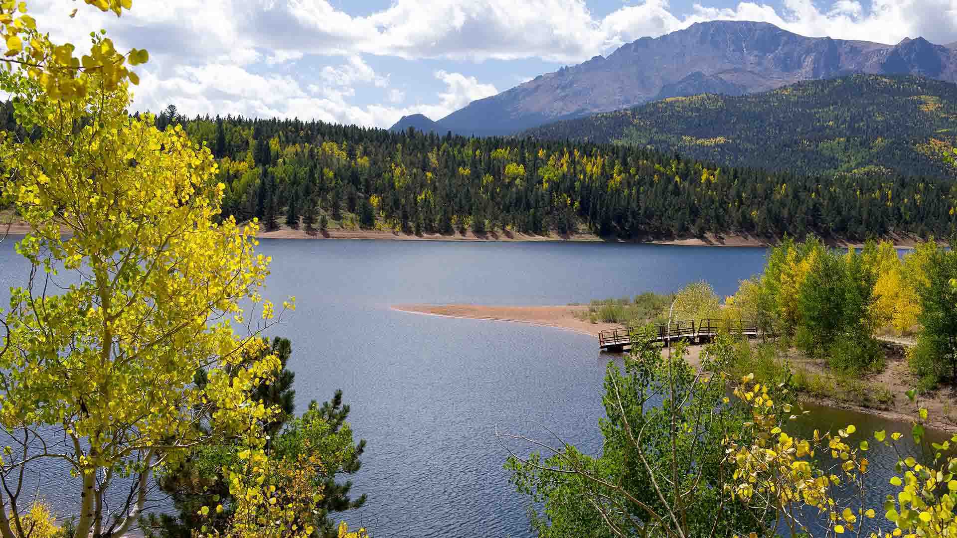 The blue waters of Crystal Creek Reservoir below Pikes Peak taken on a sunny fall day. Yellow aspens are seen dotting the hillside behind the lake.