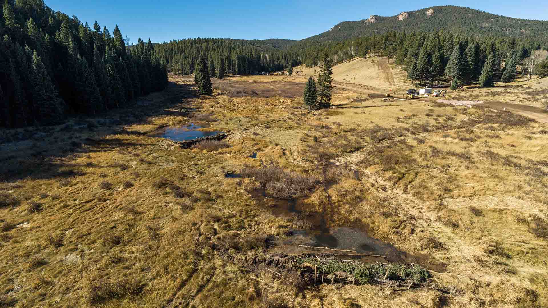 Aerial photo of a stream with multiple beaver dams blocking the flow of water in a mountainous area.