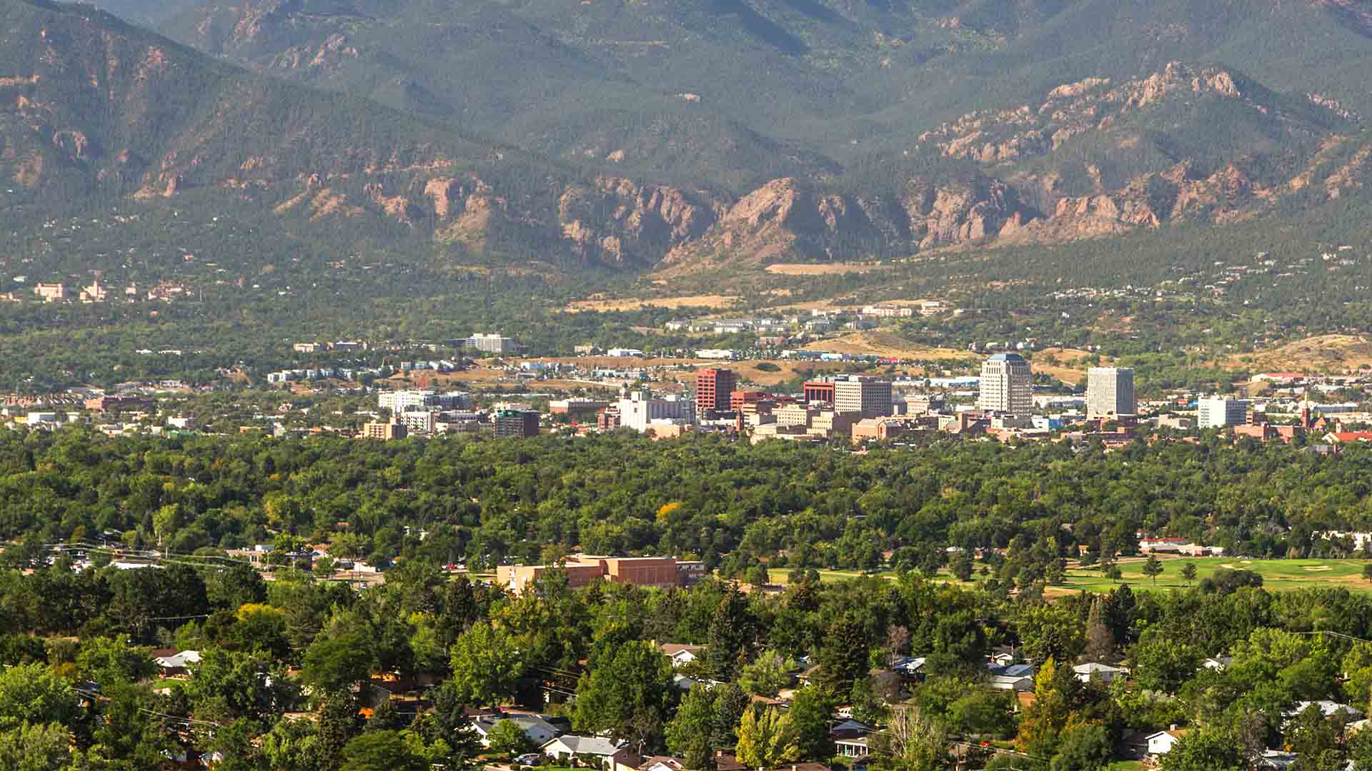 Photo of Colorado Springs skyline from a distance looking west, with the foothills in the background.