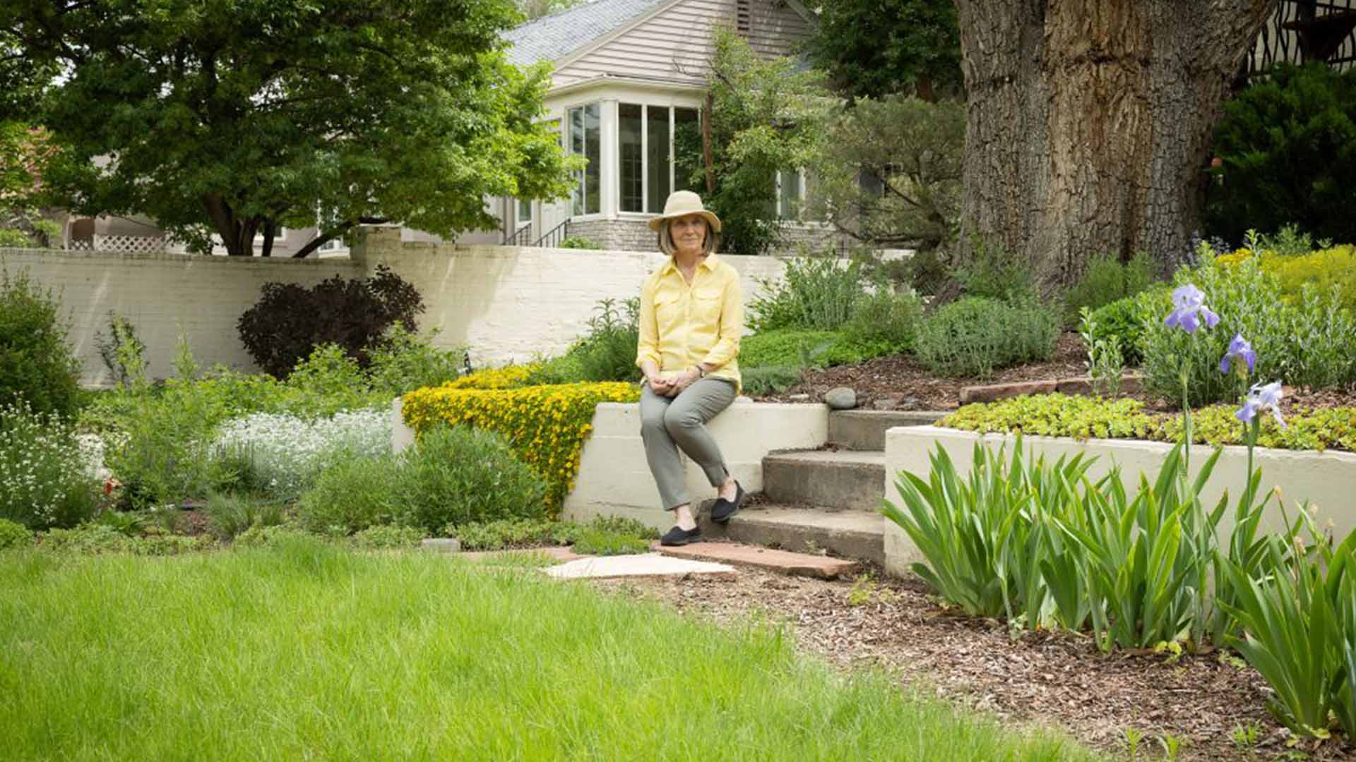 A woman sitting on a retaining wall, with a green lawn in front of her.