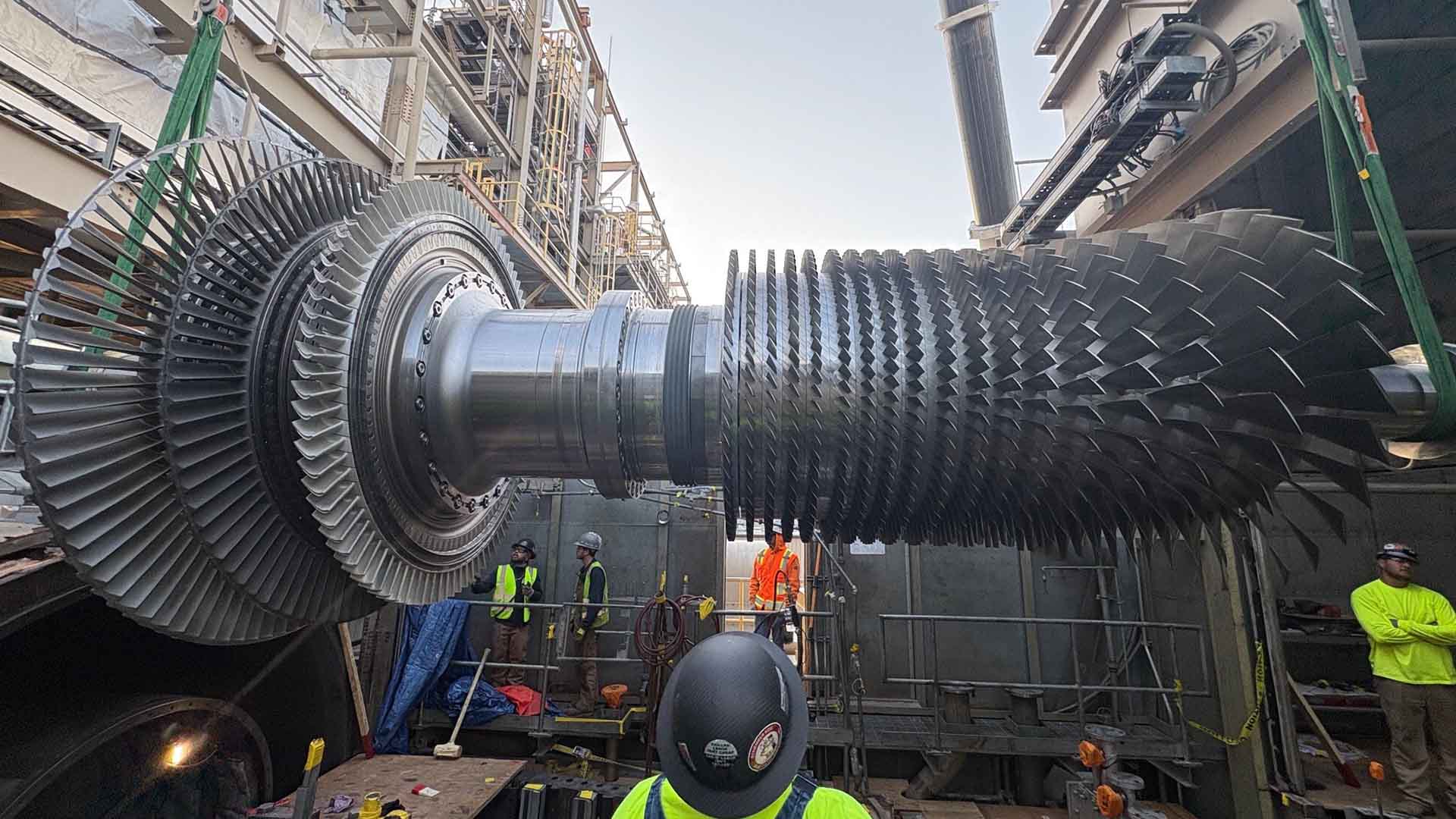 A man in a hard hat staring at an extremely large industrial rotor.
