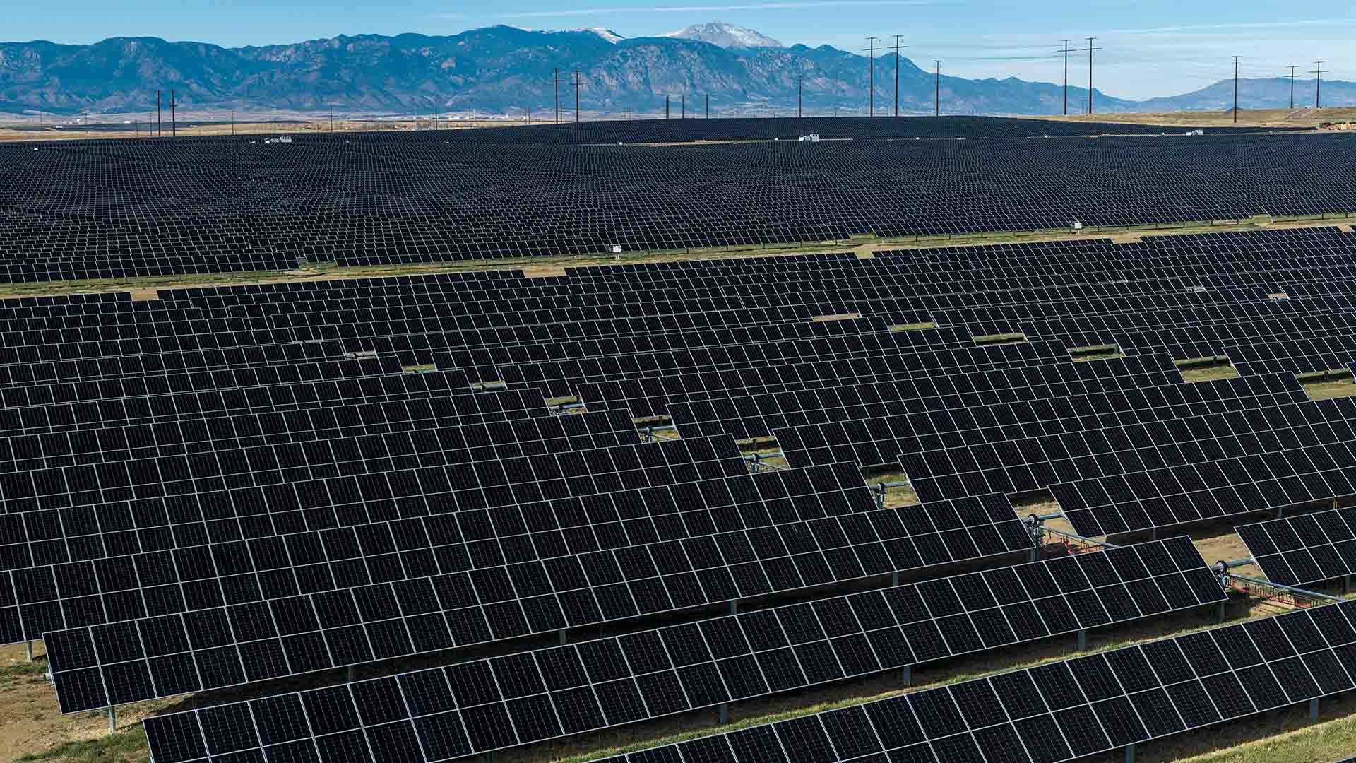 Aerial image of a many rows of solar panels with Pikes Peak visible in the distance.