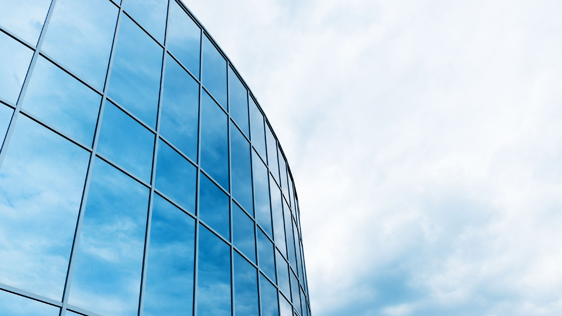 Primer plano de las ventanas de cristal de un edificio de oficinas en las que se refleja un cielo nublado.