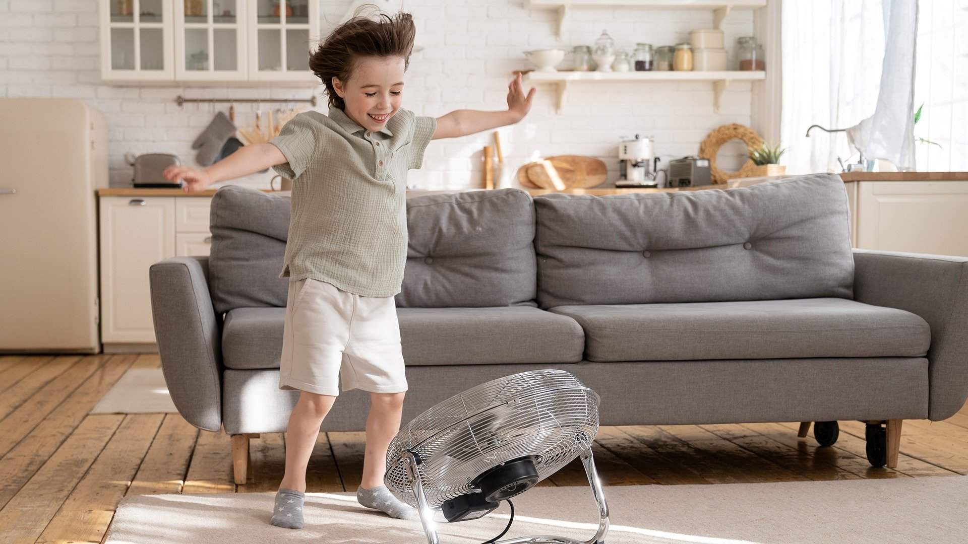 A child standing in front of a fan with his arms out.